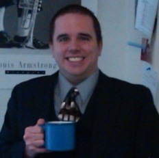 Picture of former student Keven D. dressed in a buisiness suit holding coffee