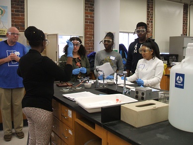 Students in a science lab looking at an instructor demonstrating a procedure